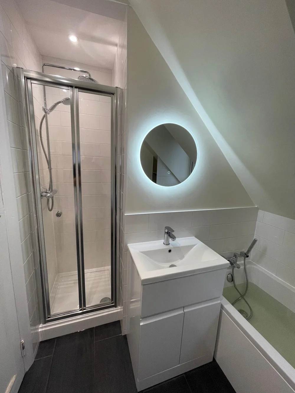 Compact loft shower room with backlit round mirror and bi-fold shower door — bathroom renovation