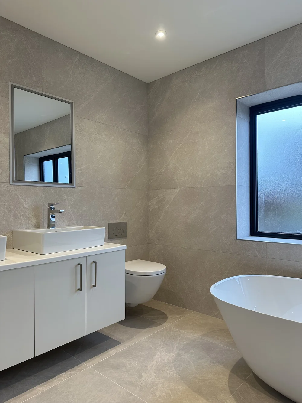 Contemporary stone-tiled bathroom with freestanding bath, floating vanity and twin basins — bathroom renovation