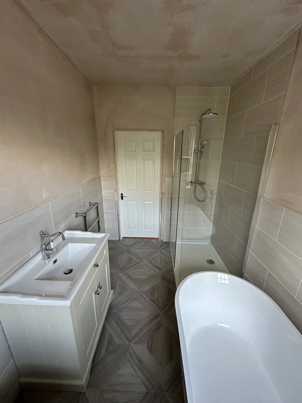Family bathroom mid-renovation with fresh plaster, shaker vanity, walk-in shower and freestanding bath — bathroom renovation