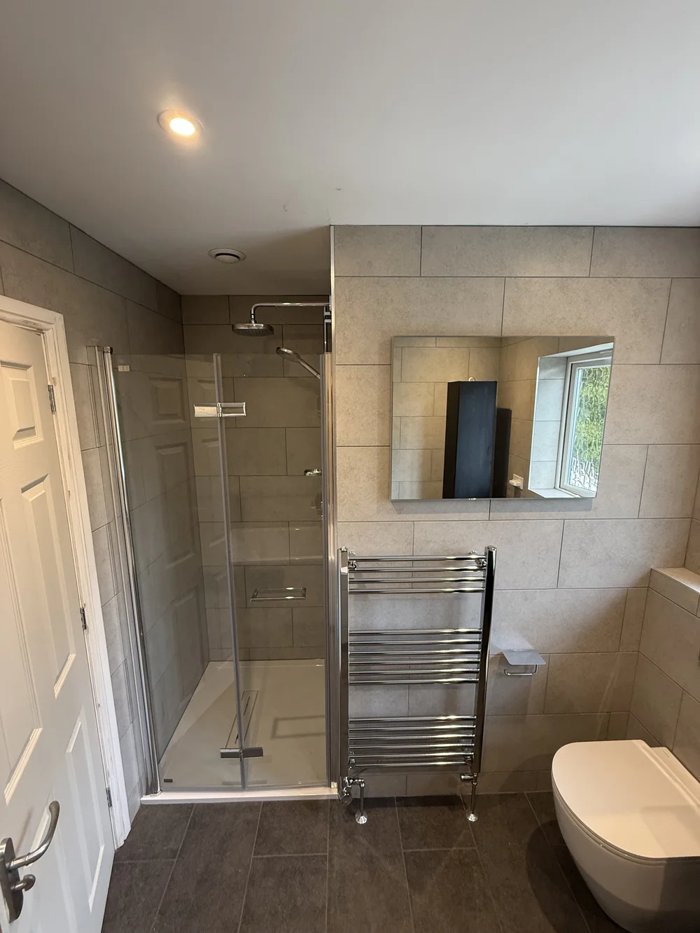 Stone-tiled family bathroom with hinged glass shower enclosure and chrome towel rail — bathroom installation in Reading