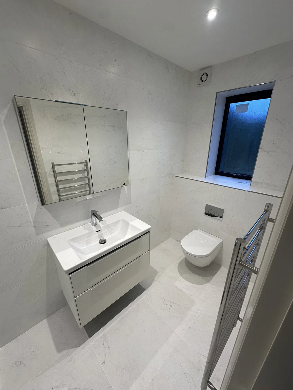 White marble ensuite with wall-hung vanity, mirrored cabinet and back-to-wall WC — Reading