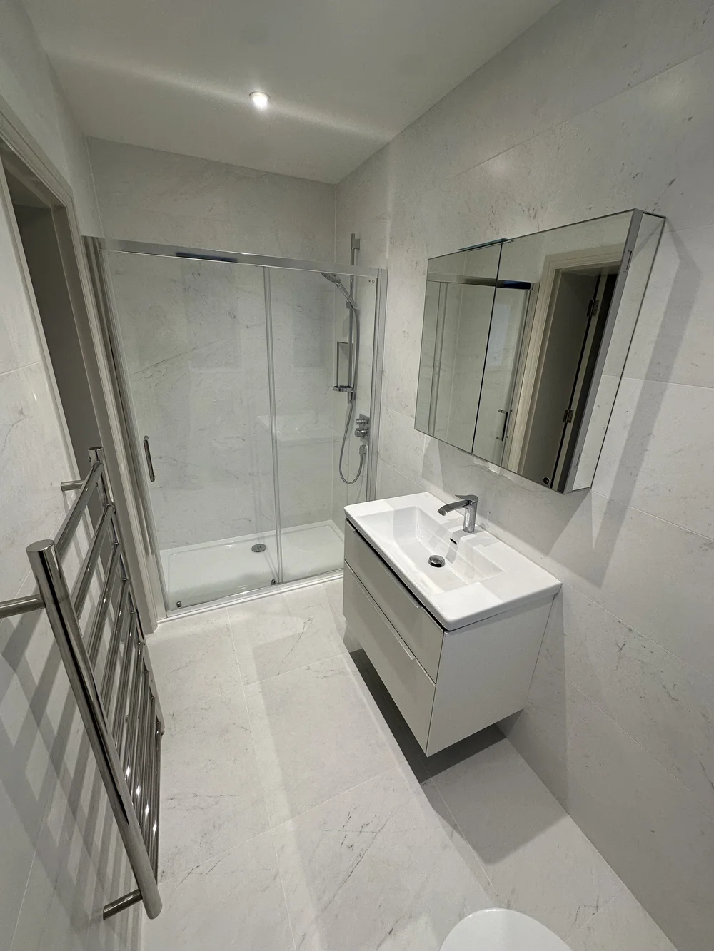 White marble shower room with sliding enclosure, wall-hung vanity and heated ladder rail — bathroom installation