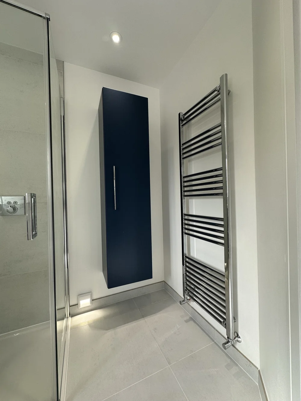 Detail of navy wall-hung storage cabinet with chrome ladder radiator — bathroom design