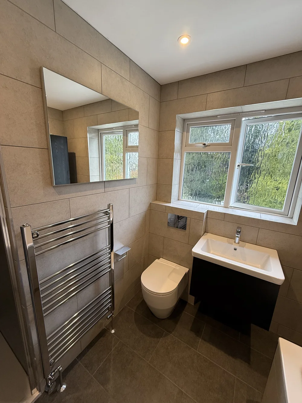 Beige-tiled bathroom with wall-hung black vanity and chrome heated rail — bathroom renovation