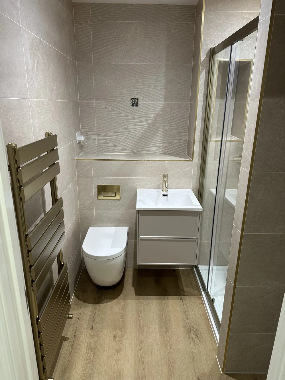 Textured stone shower room with brushed brass trim and designer towel rail — bathroom installation