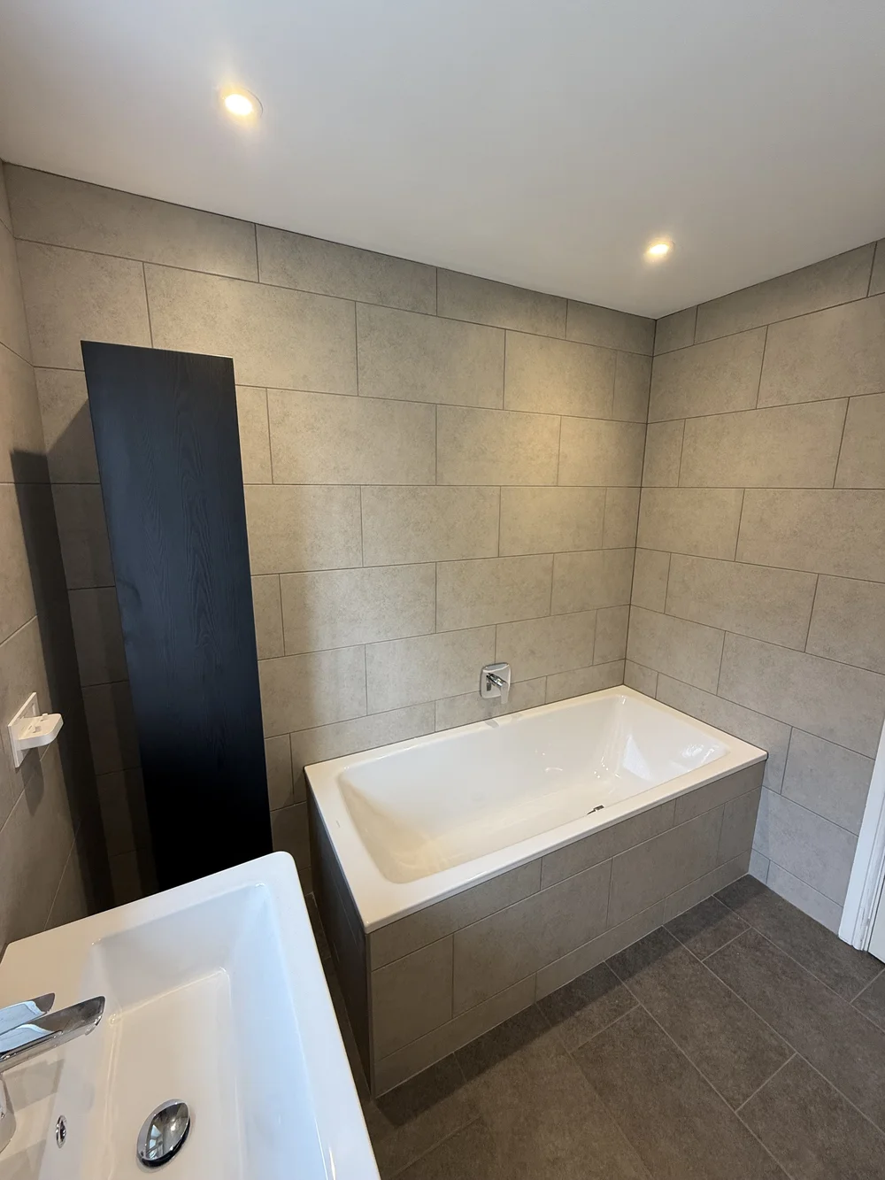 Stone-tiled bathroom with panelled bath and tall black storage column — bathroom renovation