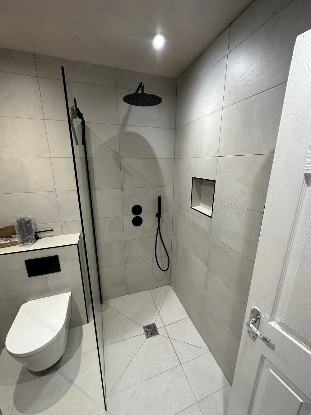 Stone-tiled walk-in shower with matte black rainfall head and recessed niche — wet room in Reading
