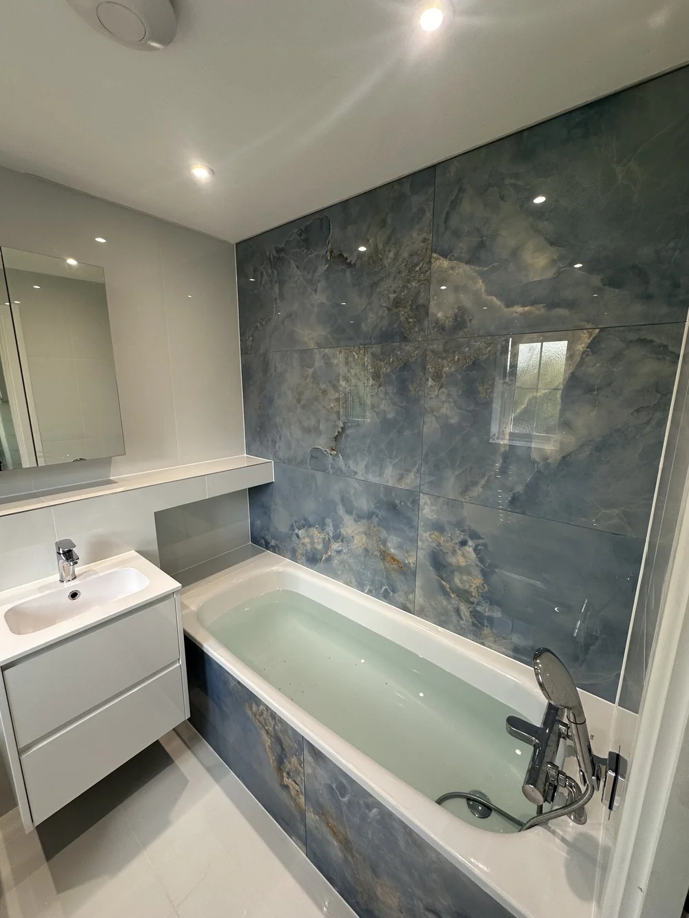 Family bathroom with blue onyx-effect feature wall, panelled bath and floating white vanity — bathroom installation