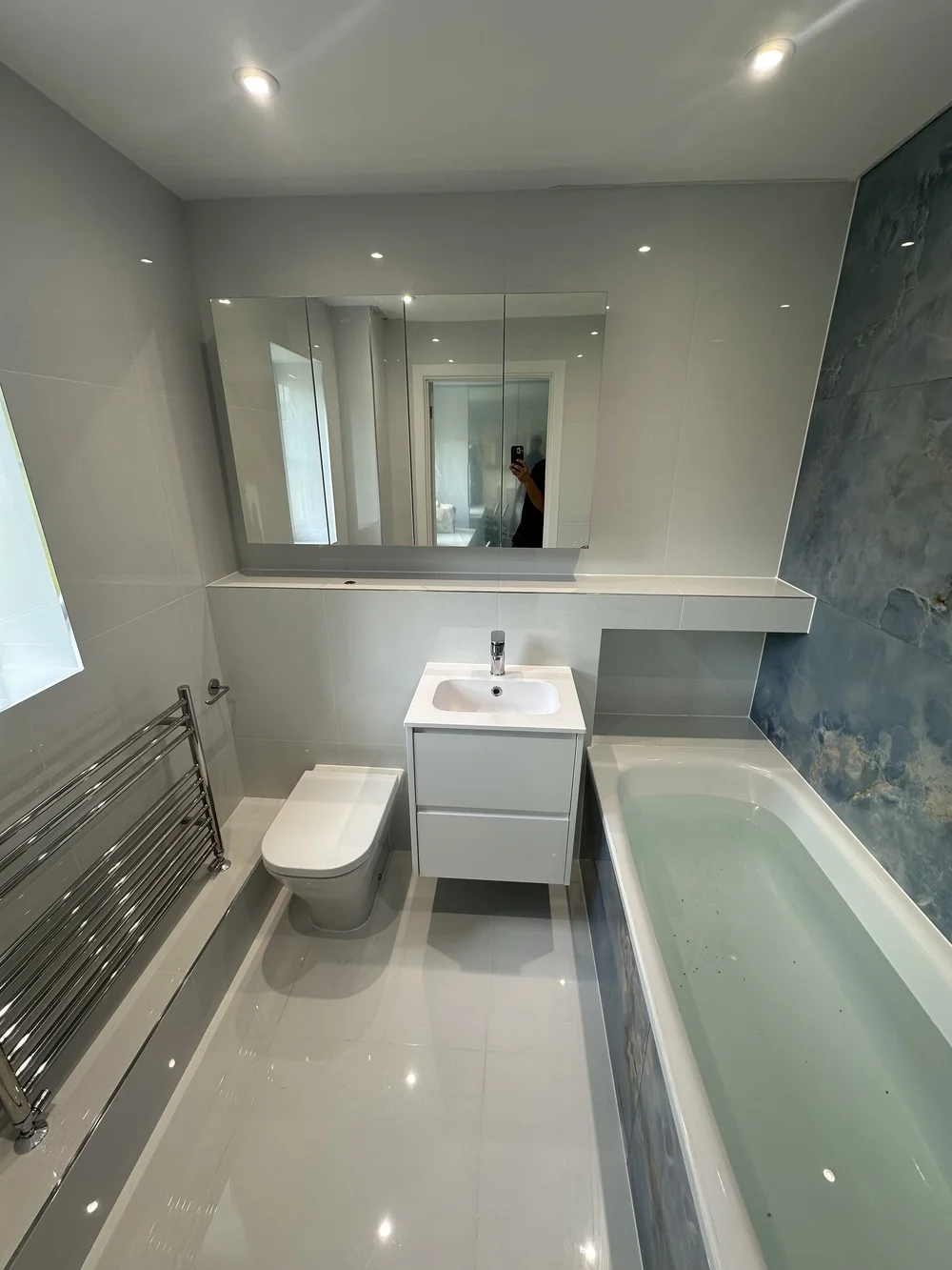 Bright family bathroom with mirrored cabinet, white vanity and blue onyx accent wall — bathroom renovation in Reading