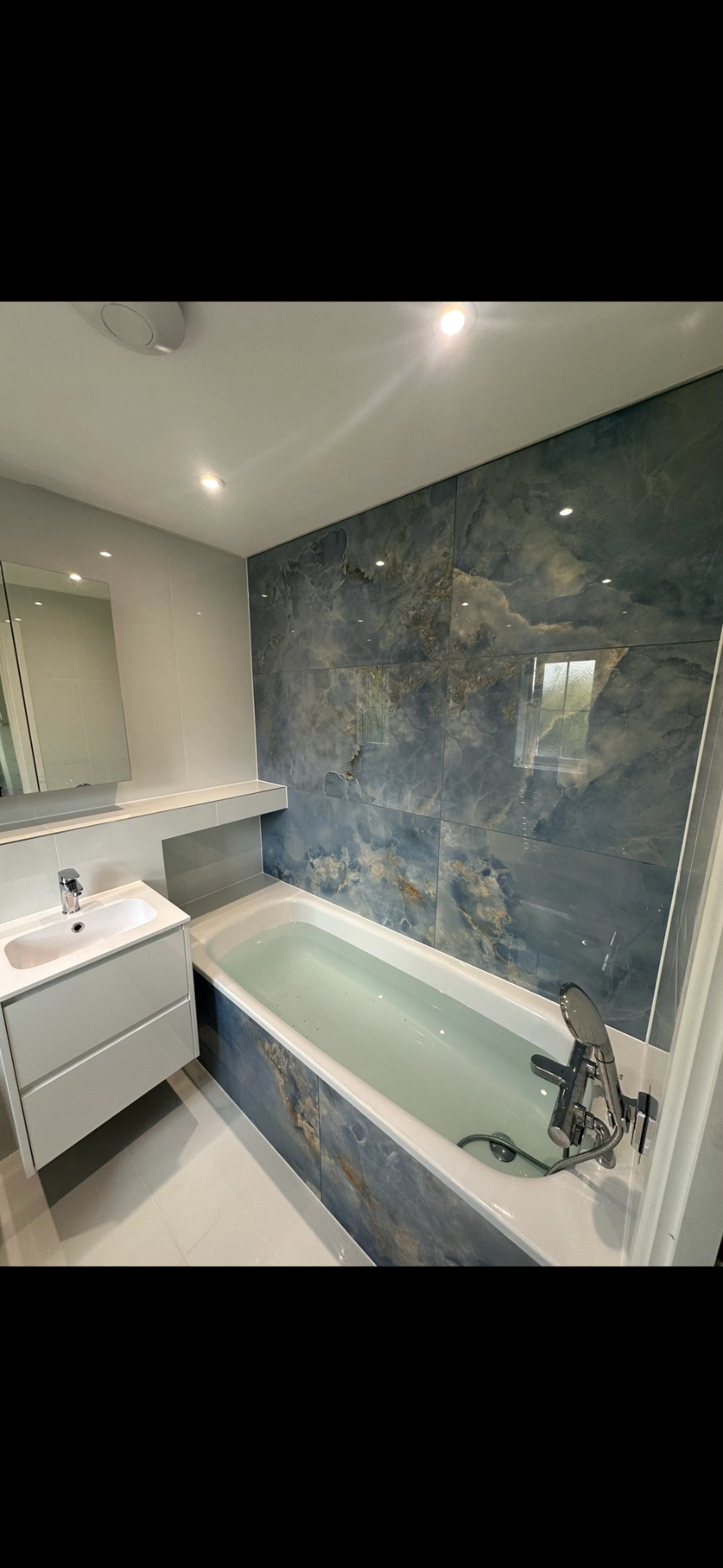 Bathroom with blue onyx-effect feature wall, panelled bath and floating white vanity — bathroom renovation