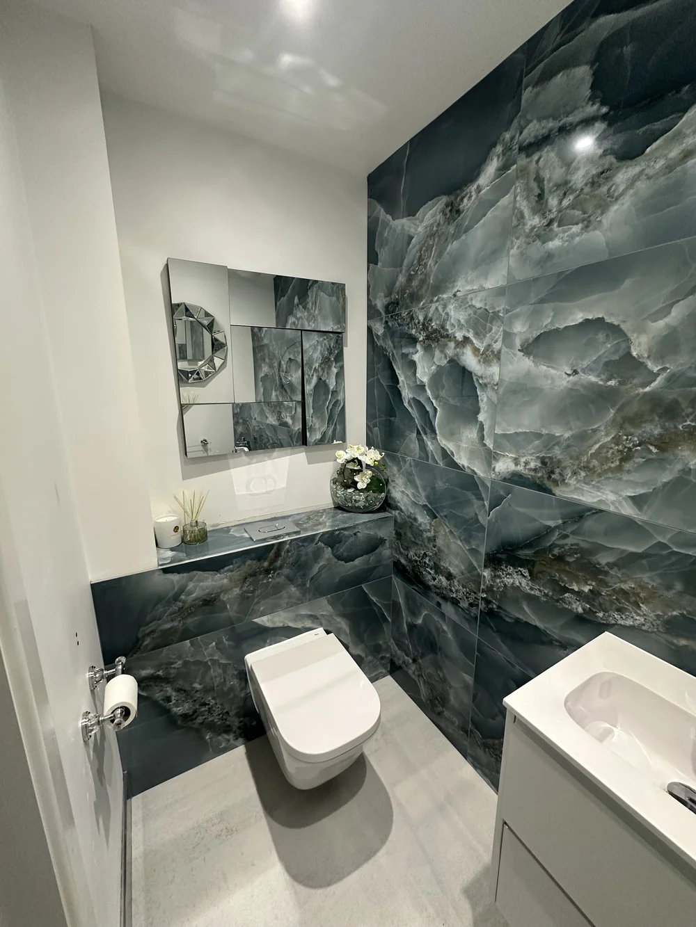Bespoke cloakroom with full-height blue onyx feature wall and faceted mirror — bathroom design