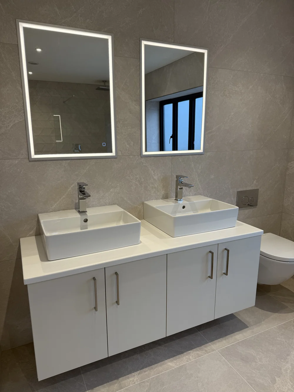 Twin countertop basins with LED mirrors on wall-hung vanity — ensuite installation