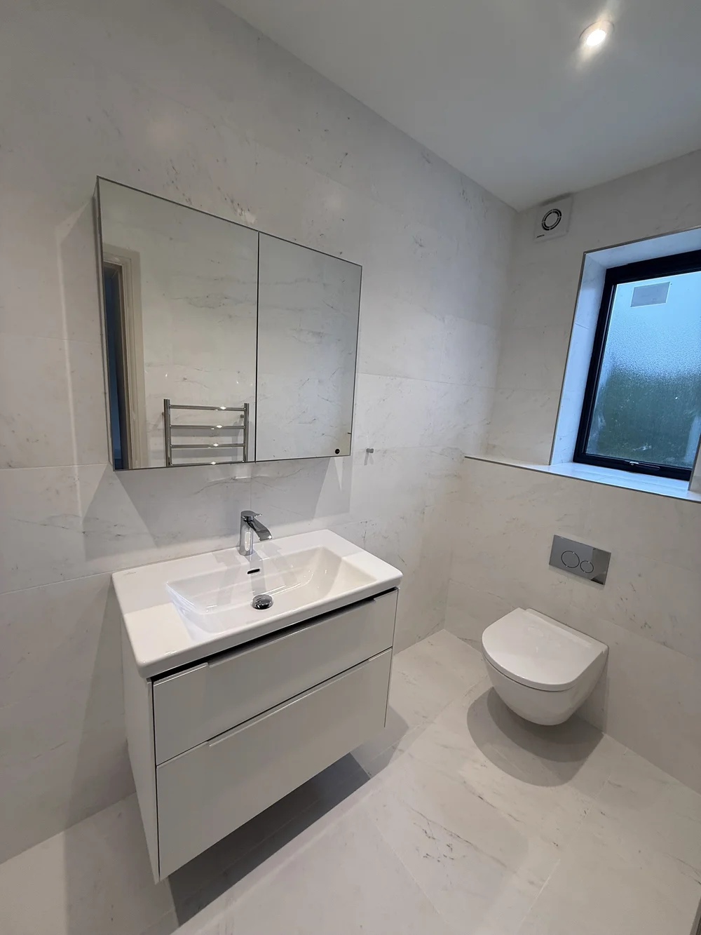 White marble family bathroom with wall-hung vanity and concealed cistern
