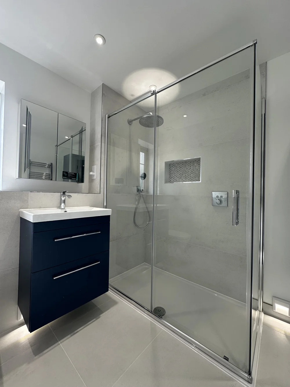 Modern ensuite with navy floating vanity, mirrored cabinet and sliding-door shower enclosure — bathroom installation