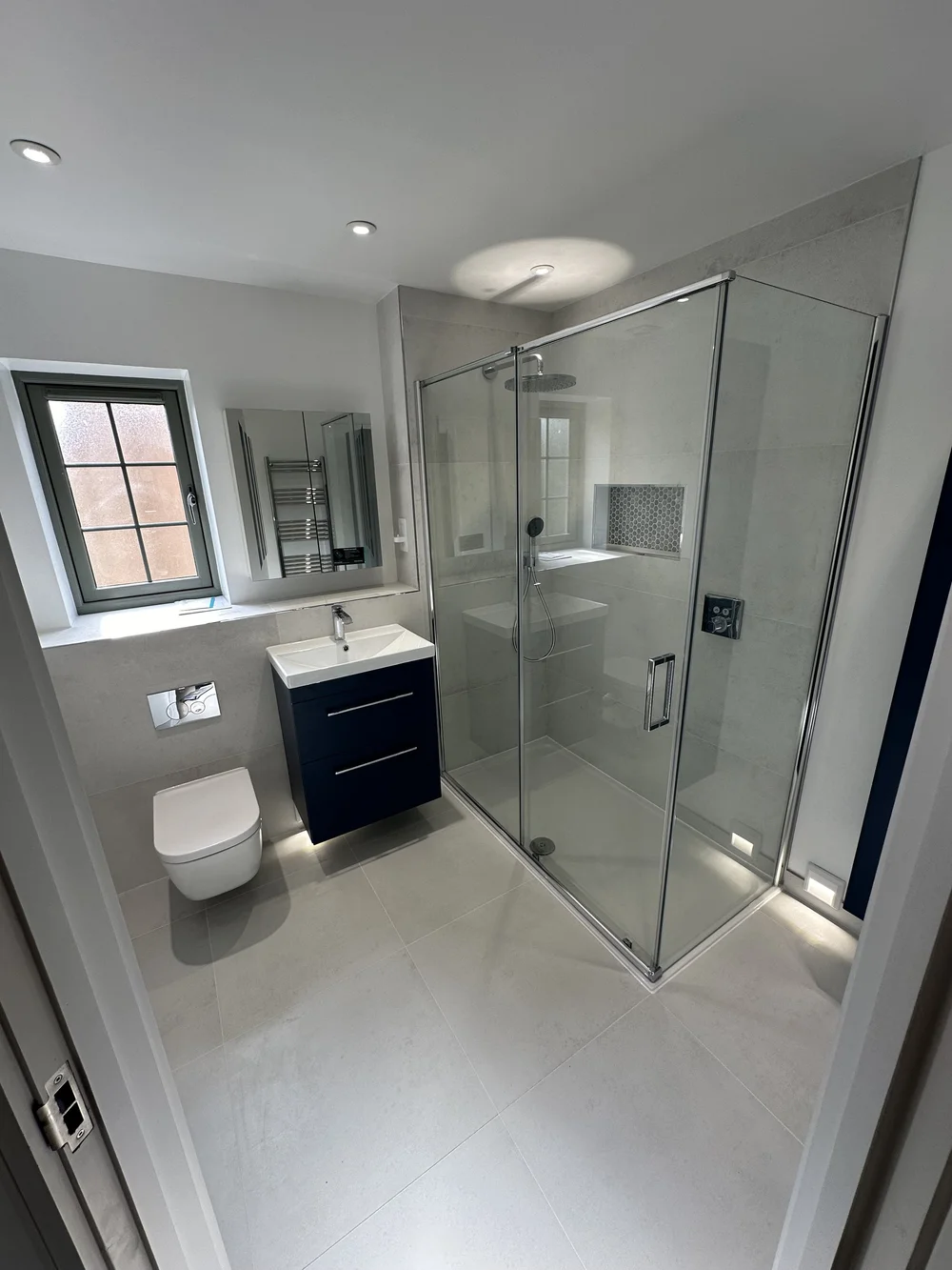 Fitted ensuite with navy vanity, wall-hung WC and corner shower enclosure — bathroom installation in Reading
