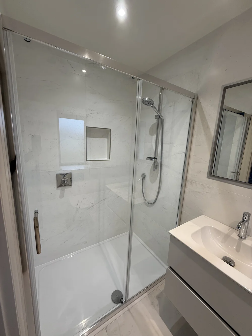 Marble shower enclosure with sliding door and recessed niche — bathroom renovation