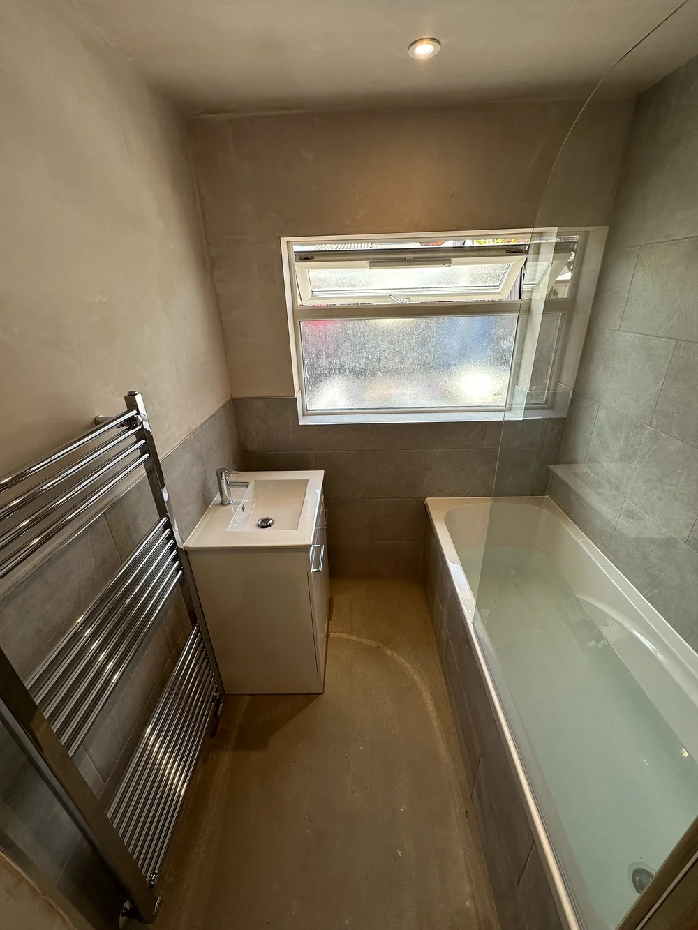 Compact family bathroom mid-renovation with fresh plaster, stone tiling and new bath — bathroom renovation