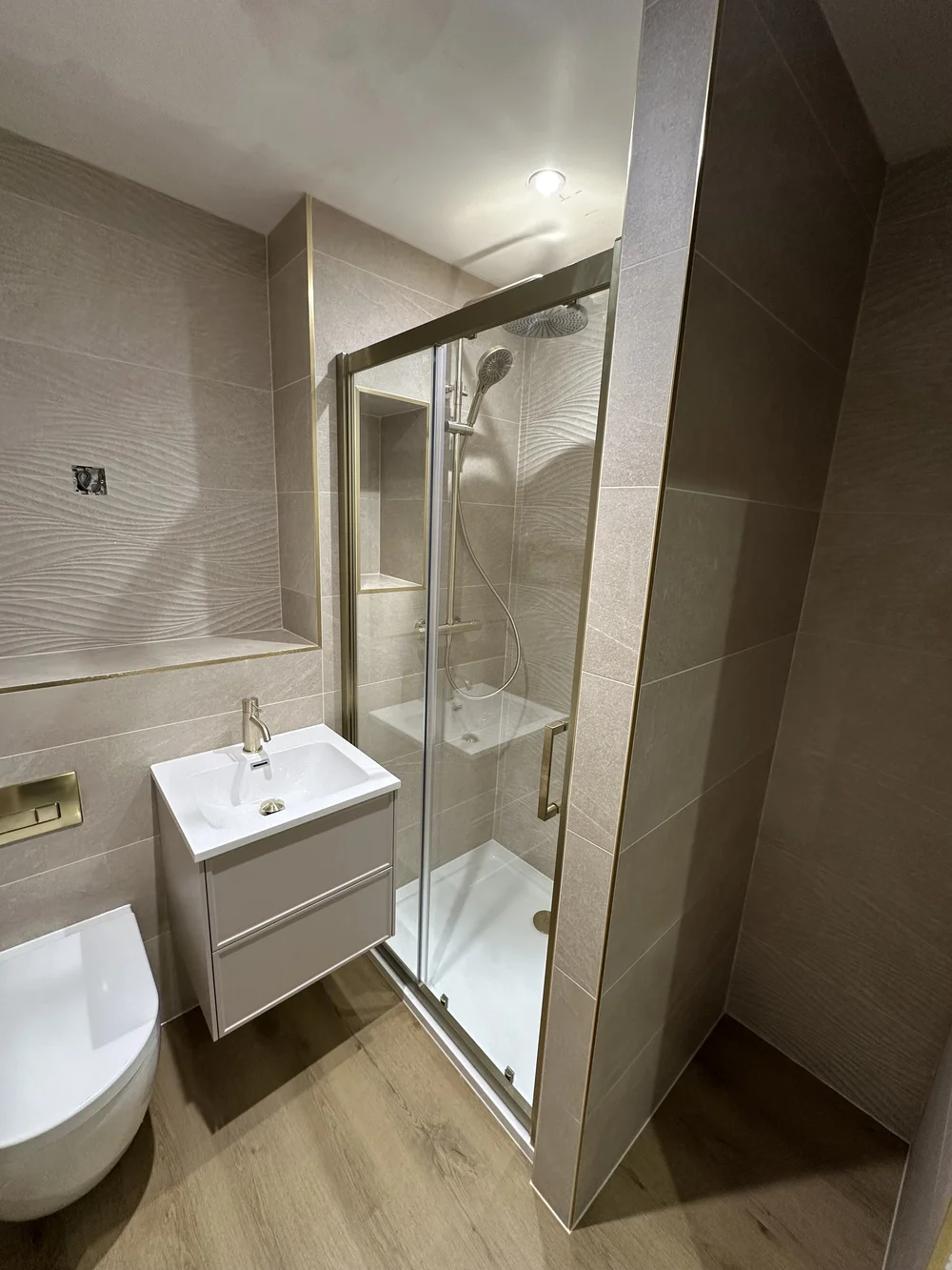 Wave-tiled shower room with brushed brass fittings and oak-effect floor — bathroom renovation