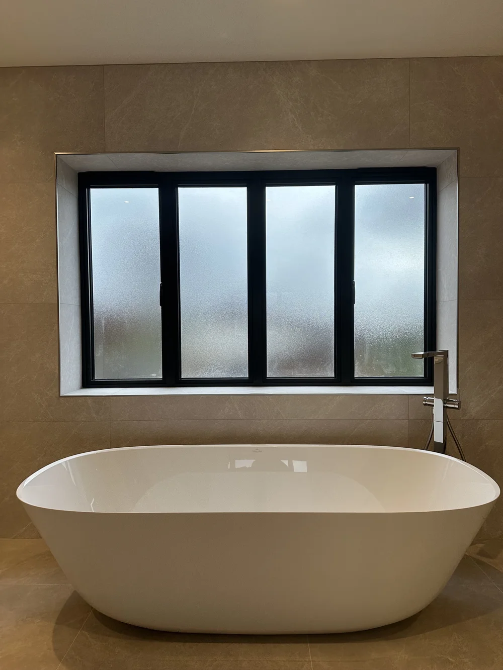 Freestanding stone-resin bath under crittall window in marble master bathroom — bathroom installation
